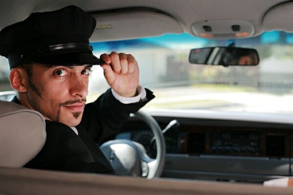 Portrait of a handsome male chauffeur sitting in a car saluting a passanger